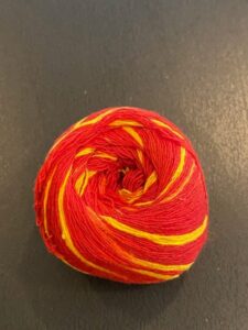  A tightly wound roll of red and yellow Mauli Kalawa cotton thread placed on a dark surface